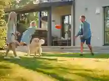 Familie mit Hund spielt Frisbee vor ihrem Haus Familie mit Hund spielt Frisbee vor ihrem Haus