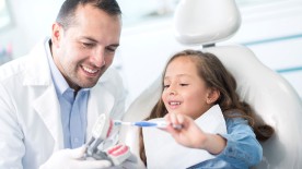 Versicherungen für Zahnärzte: Zahnarzt zeigt einem kleinen Mädchen, wie man Zähne putzt. Versicherungen für Zahnärzte: Zahnarzt zeigt einem kleinen Mädchen, wie man Zähne putzt.