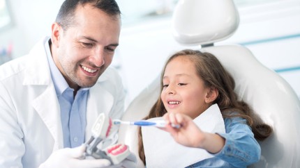 Versicherungen für Zahnärzte: Zahnarzt zeigt einem kleinen Mädchen, wie man Zähne putzt. Versicherungen für Zahnärzte: Zahnarzt zeigt einem kleinen Mädchen, wie man Zähne putzt.