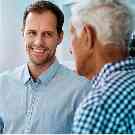 Assistanceleistungen bei der Pflege von Angehörigen: Junger Mann lächelt älteren Mann an