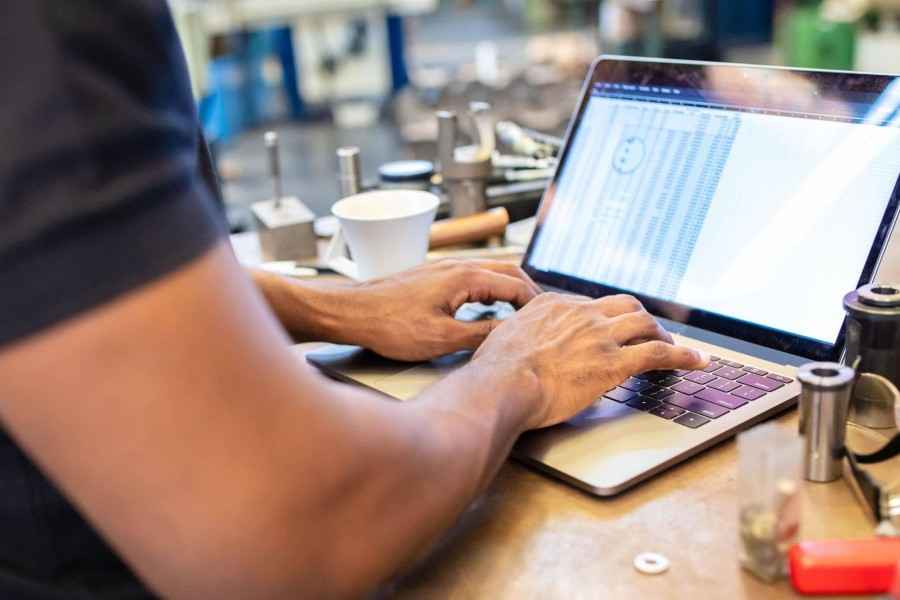 Fokusbranche Maschinenbau und Metallverarbeitung, Zusatzbaustein Cyber-Versicherung: Mitarbeiter tippt in Produktionshalle tippt Produktionszahlen in Notebook ein.