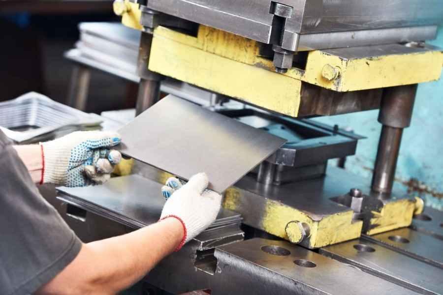 Fokusbranche Maschinenbau und Metallverarbeitung, Haftpflicht-Baustein: Ein Mitarbeitender schiebt eine Metallplatte in eine Stanzmaschine