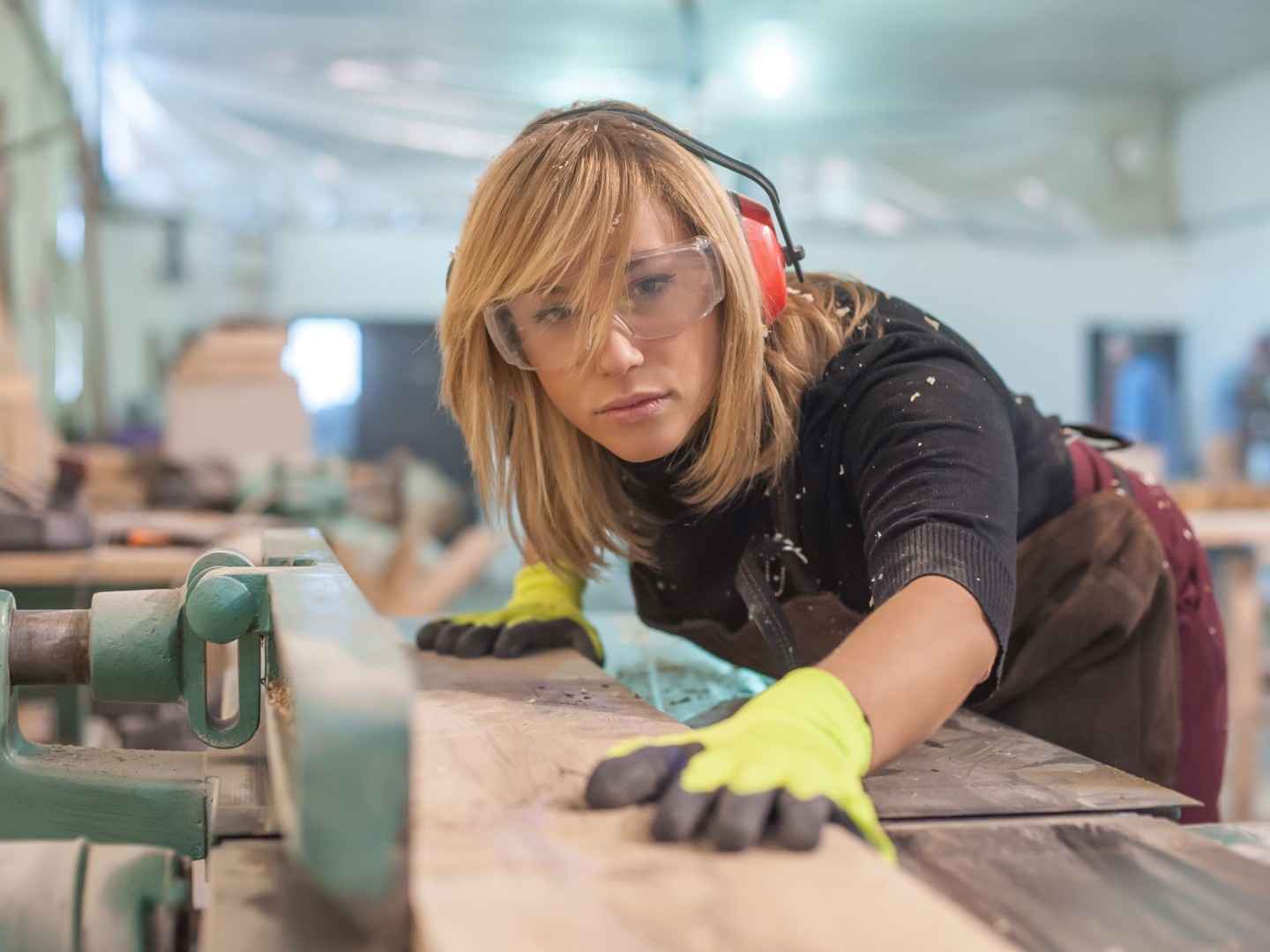 Eine Tischlerin mit Ohren- und Augenschutz sägt Holz an einer elektrischen Maschine zu