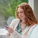 Eine junge Frau trinkt einen Kaffee und schaut dabei auf ihr Handy. 