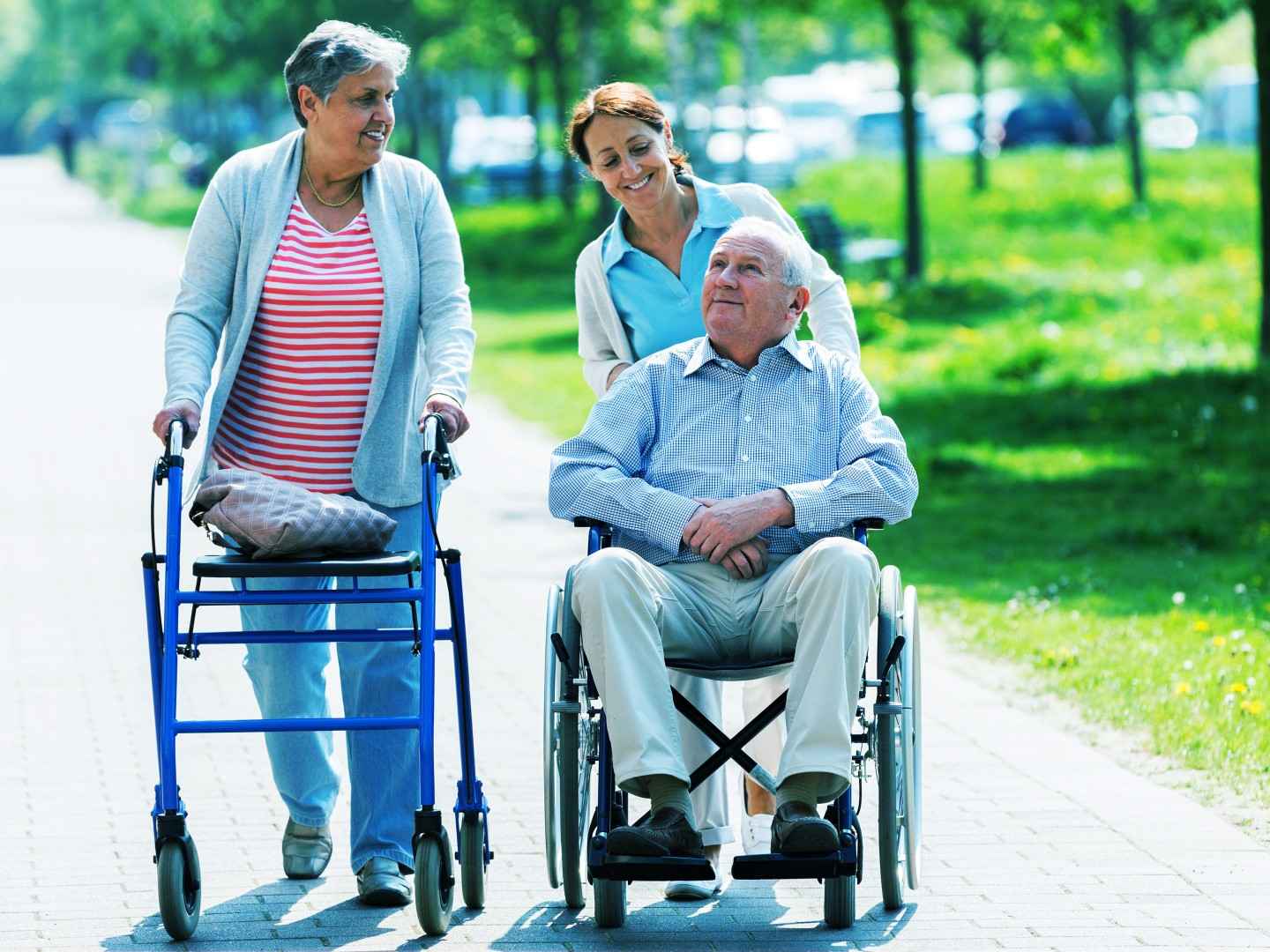 Frau mit Rollator und Mann im Rollstuhl machen einen Spaziergang.