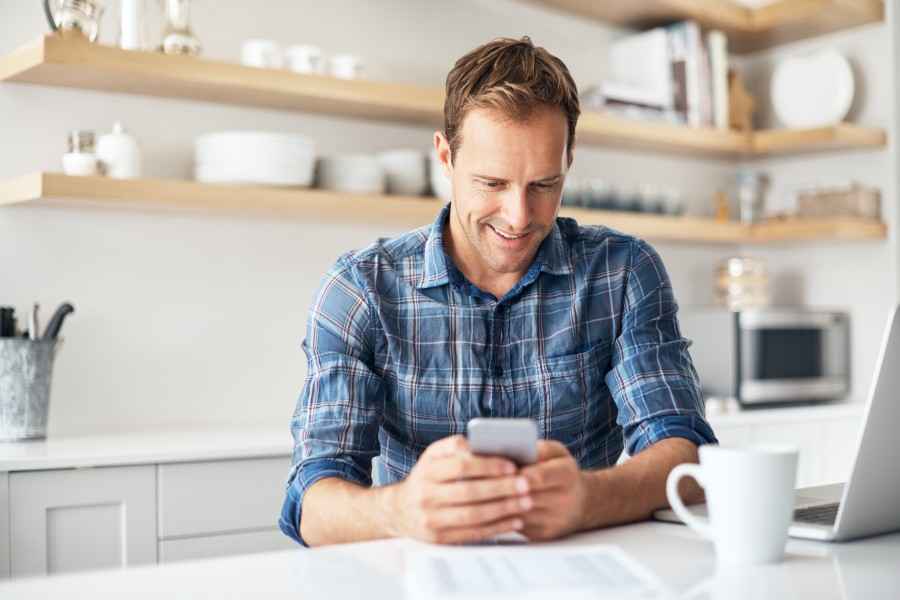 Junger Mann mit Handy in seiner Küche