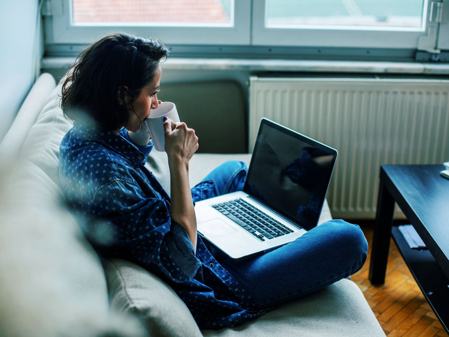 Frau mit Laptop auf Sofa trinkt Tee
