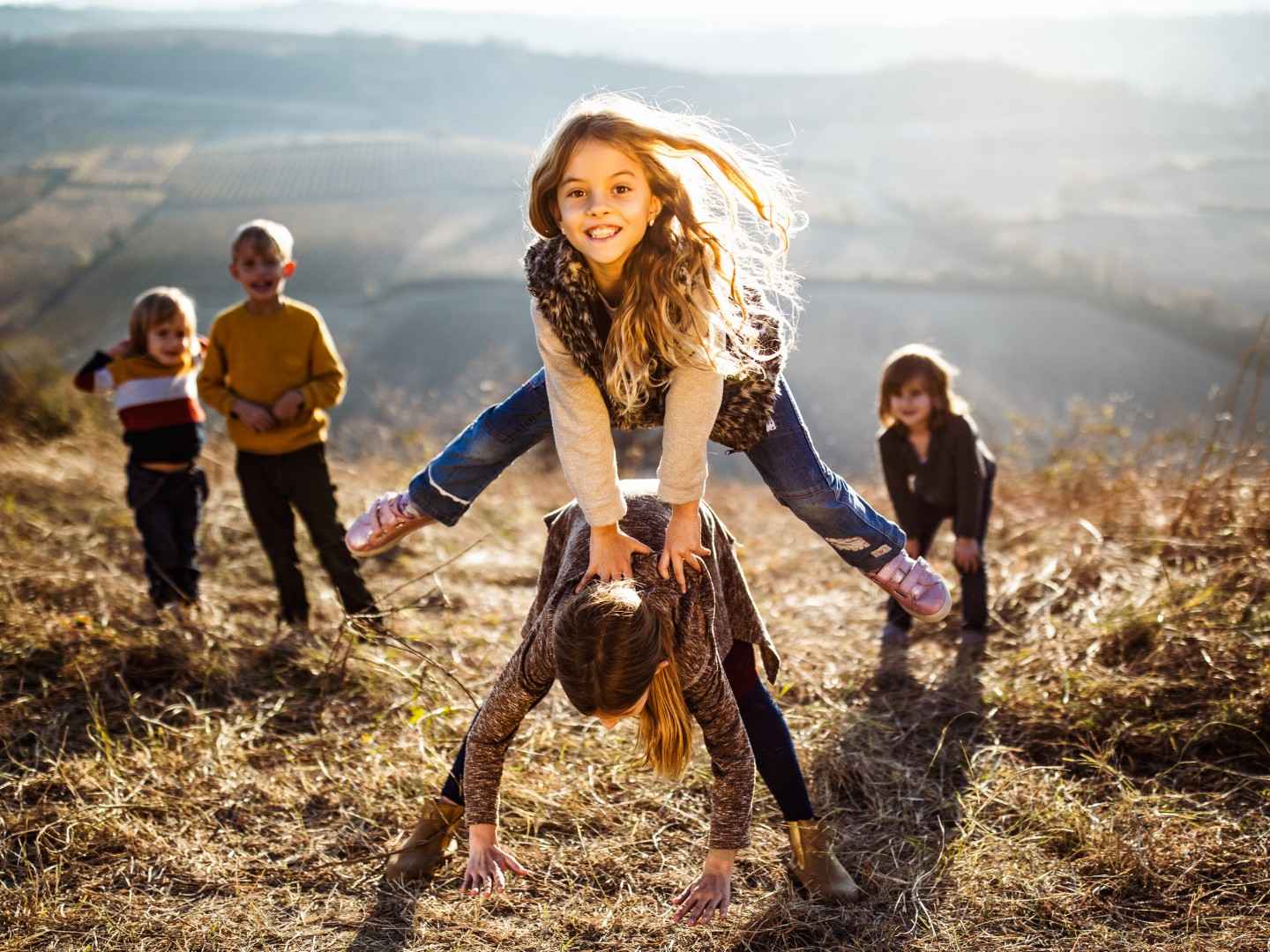 Kinder spielen auf einer Wiese und machen Bockspringen