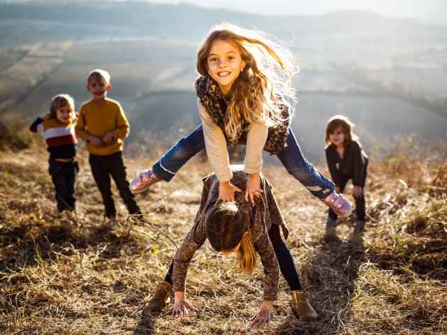 Kinder spielen auf einer Wiese und machen Bockspringen
