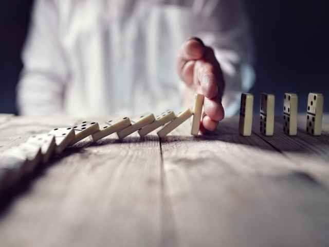 Hand unterbricht Linie von fallenden Dominosteinen