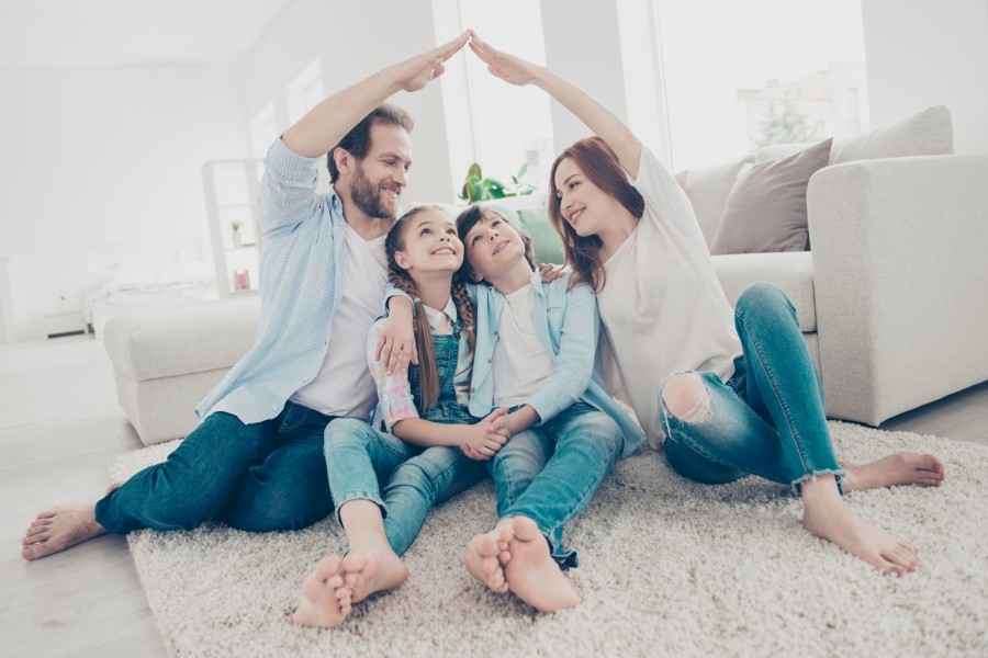 Gothaer Online-Services rund um Nachweise/Bescheinigungen im Bereich Lebensversicherungen: Familie sitzt sorgenfrei im Wohnzimmer zusammen, die Eltern formen mit ihren Armen ein schützendes Dach über ihrer Familie