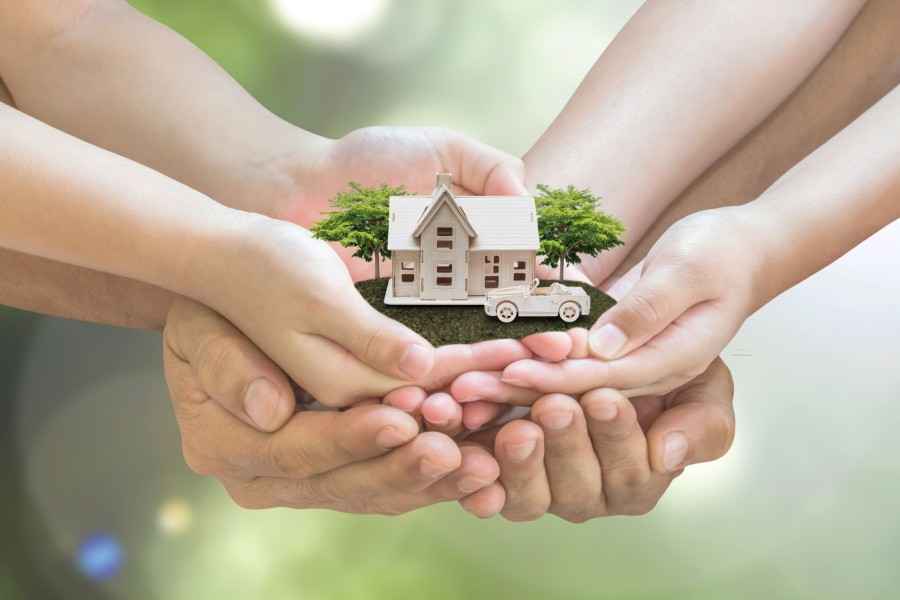 Gothaer Online-Services für Vertragsänderungen von Sachversicherungen: 3 Paar Hände sind übereinandergelegt und halten ein Miniaturhaus und ein Miniaturauto.