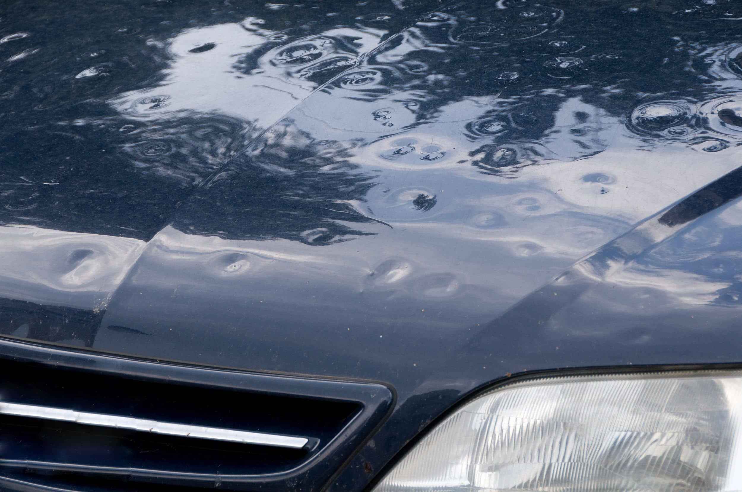 Hagelbeulen auf der Motorhaube eines dunkelblauen Autos
