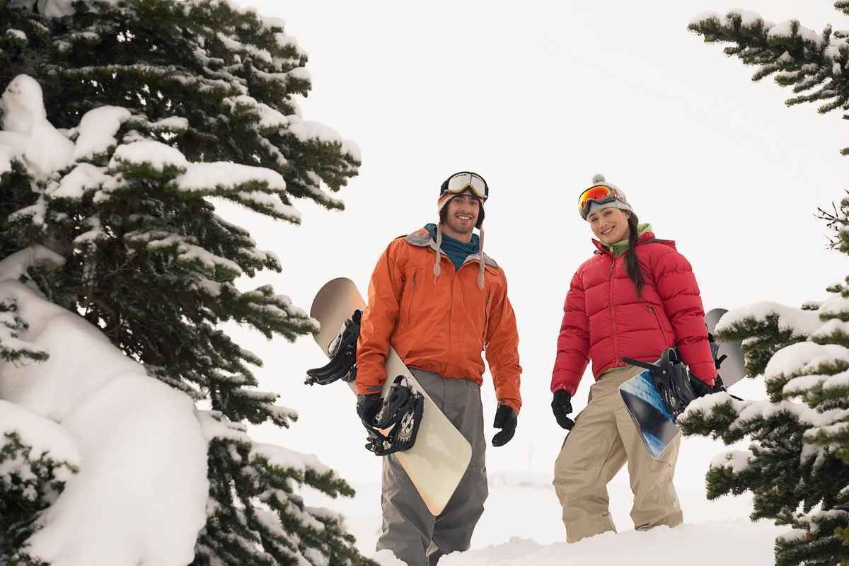 Eine junge Frau und ein junger Mann stehen mit Snowboards im Schnee.