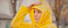 Gothaer Sturmversicherung: Junge Frau mit gelber Regenjacke ist bei Sturm unterwegs.