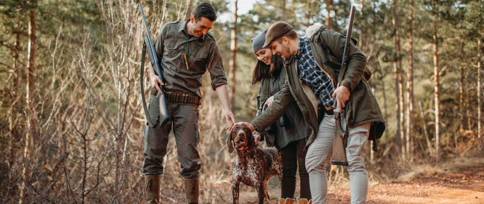 Gothaer Jagdhaftpflichtversicherung: Drei Jäger mit ihren Jagdgewehren im Arm loben ihren Jagdhund