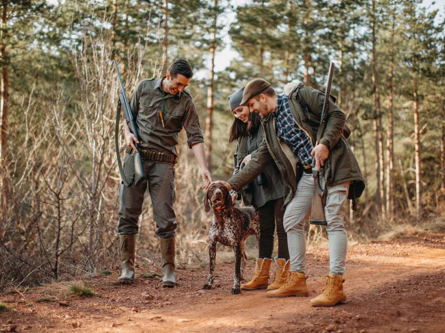 Gothaer Jagdhaftpflichtversicherung: Drei Jäger*innen mit ihren Jagdgewehren im Arm loben ihren Jagdhund