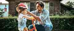 Gothaer Grundfähigkeitsversicherung für Kinder: Ein Vater zieht seiner kleinen Tochter auf einem Fahrrad einen Helm zu ihrem Schutz auf.
