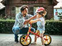 Gothaer Grundfähigkeitsversicherung für Kinder: Ein Vater zieht seiner kleinen Tochter auf einem Fahrrad einen Helm zu ihrem Schutz auf.