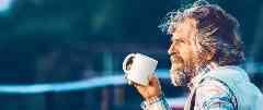 Pflegetagegeldversicherung: Älterer Herr trinkt eine Tasse Kaffee auf einer Terrasse.