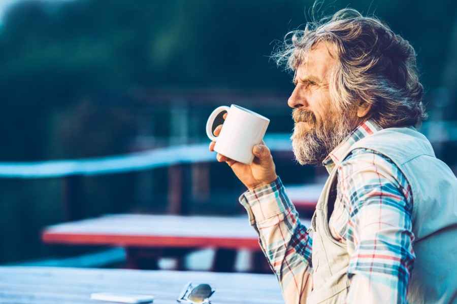 Pflegetagegeldversicherung: Älterer Herr trinkt eine Tasse Kaffee auf einer Terrasse.