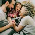 Eltern kuscheln mit Kleinkind im Bett