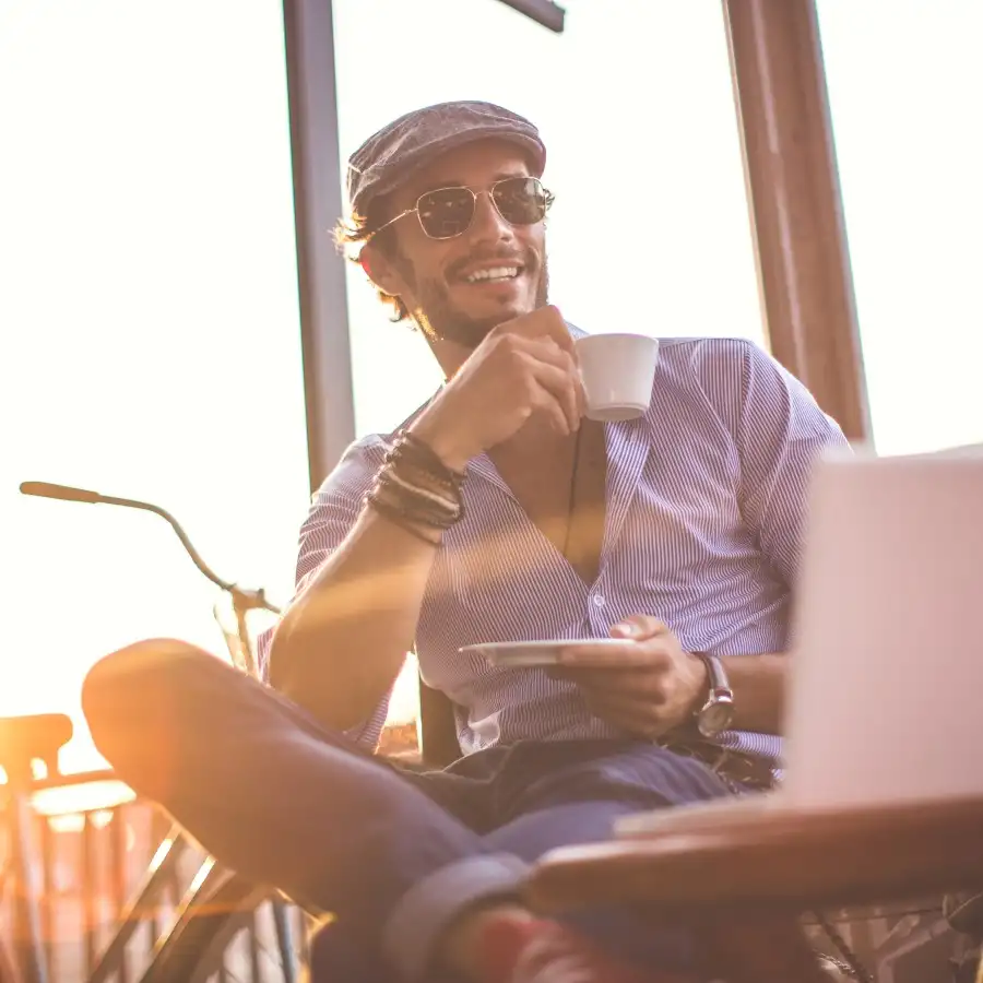 Gothaer Direktversicherung: Lässiger Typ trinkt Kaffee vor dem Laptop.