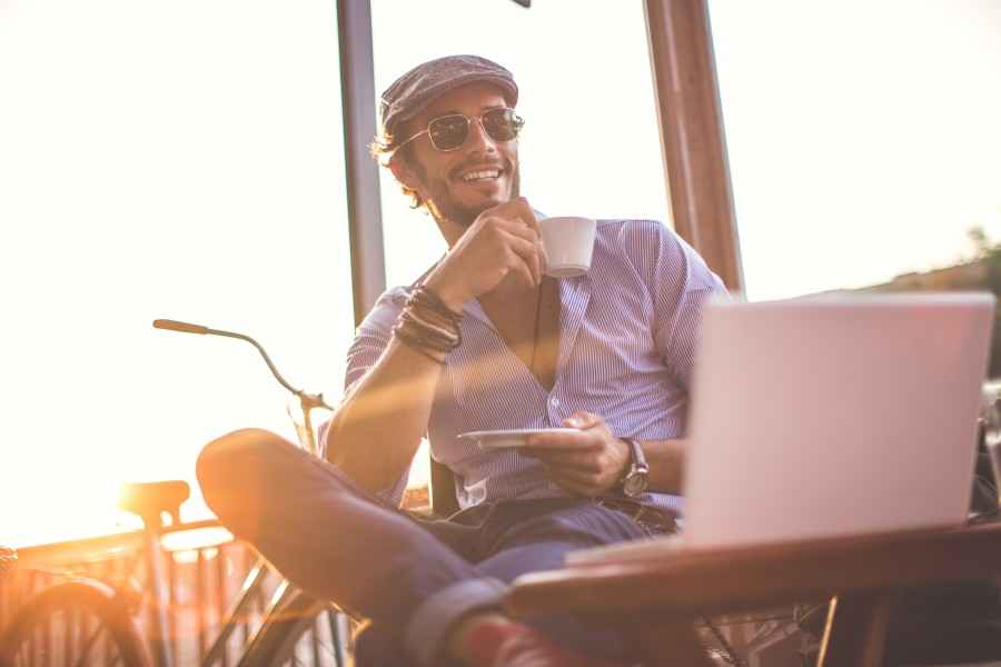 Gothaer Direktversicherung: Lässiger Typ trinkt Kaffee vor dem Laptop.