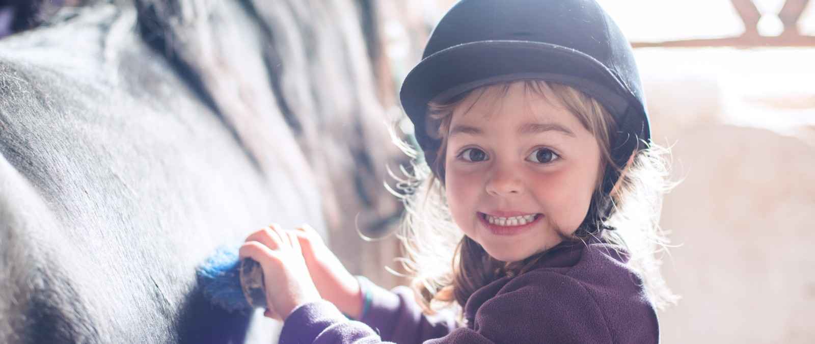 Gothaer Pferdeversicherung: Kleines Mädchen striegelt mit großer Begeisterung ein Pferd.