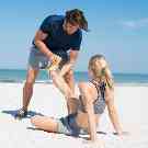 Gothaer Unfallversicherung: Jogger schaut sich am Strand den Fuß seiner Freundin an.