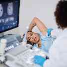 Eine Ärztin untersucht eine Frau mit einem Ultraschallgerät an der Achselhöhle. 