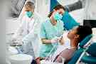 Frau liegt beim Zahnarzt auf einem Behandlungsstuhl. Ihre Zähne werden von einem Zahnarzt und einer Zahnarzthelferin behandelt.