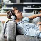 Gothaer Ratgeber Stressbewältigung: Ein junger Mann liegt auf einer Couch, hört Musik und entspannt dabei.