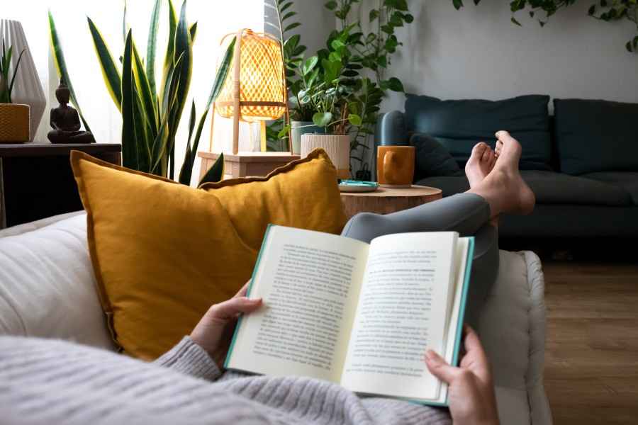 Frau ruht sich auf dem Sofa aus und liest dabei ein Buch.