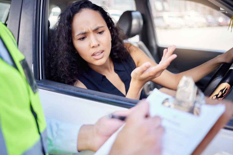 Gothaer Ratgeber Auto Bußgeldkatalog: Junge Frau am Steuer ihres Autos erhält ein Bußgeld wegen eines Verkehrsverstoßes.