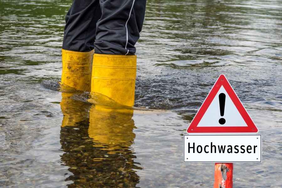 Ausschnitt von Beinen in Gummistiefeln neben Hochwasser-Schild im Hochwasser