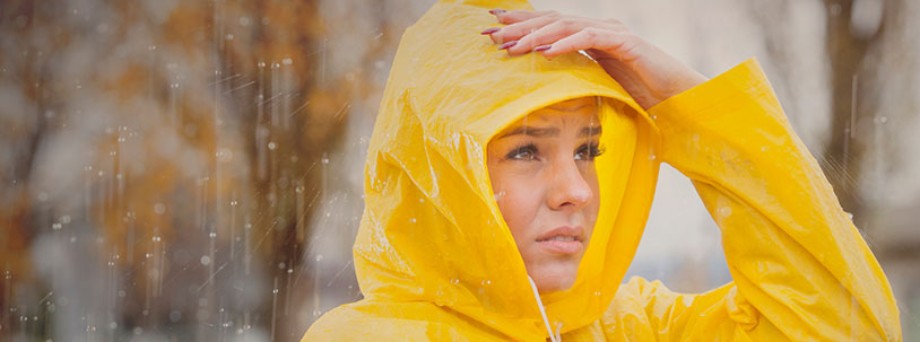 Sturmversicherung: Junge Frau mit gelber Regenjacke ist bei Sturm unterwegs. Sturmversicherung: Junge Frau mit gelber Regenjacke ist bei Sturm unterwegs.