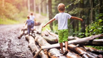 Gothaer Waldversicherung: Kinder balancieren auf Baumstämmen im Wald. Gothaer Waldversicherung: Kinder balancieren auf Baumstämmen im Wald.