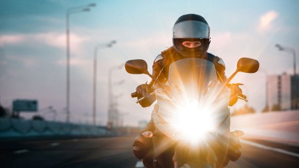 Gothaer Motorradversicherung: Motorradfahrer fährt in der Dämmerung mit seinem Motorrad auf der Straße. Gothaer Motorradversicherung: Motorradfahrer fährt in der Dämmerung mit seinem Motorrad auf der Straße.
