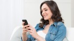 GesundheitsApp: Junge Frau sitzt mit dem Smartphone auf dem Sofa und lädt sich die App herunter. GesundheitsApp: Junge Frau sitzt mit dem Smartphone auf dem Sofa und lädt sich die App herunter.