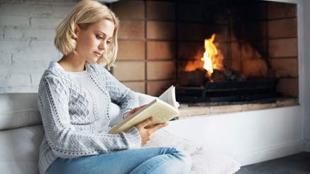 Ratgeber Brandschutz: Frau liest auf dem Sofa vor einem Kamin. Ratgeber Brandschutz: Frau liest auf dem Sofa vor einem Kamin.